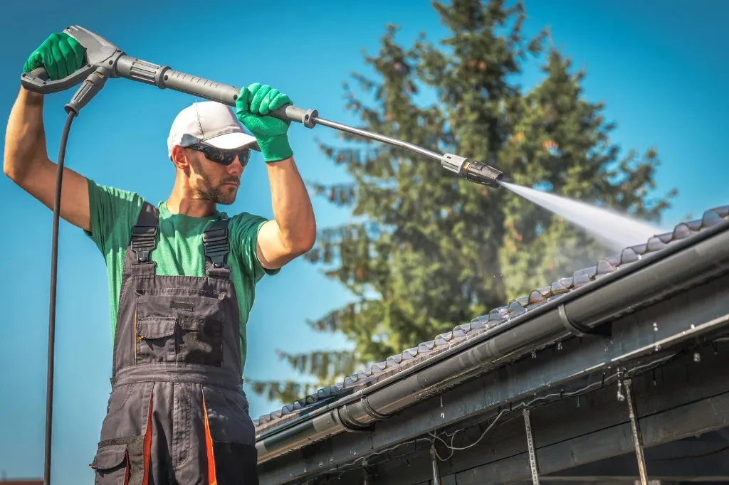 Professional worker power washing a roof under a clear blue sky
